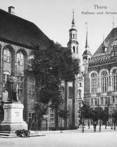 Historisches Rathaus mit Statue und Bäumen, umgeben von alten Gebäuden.